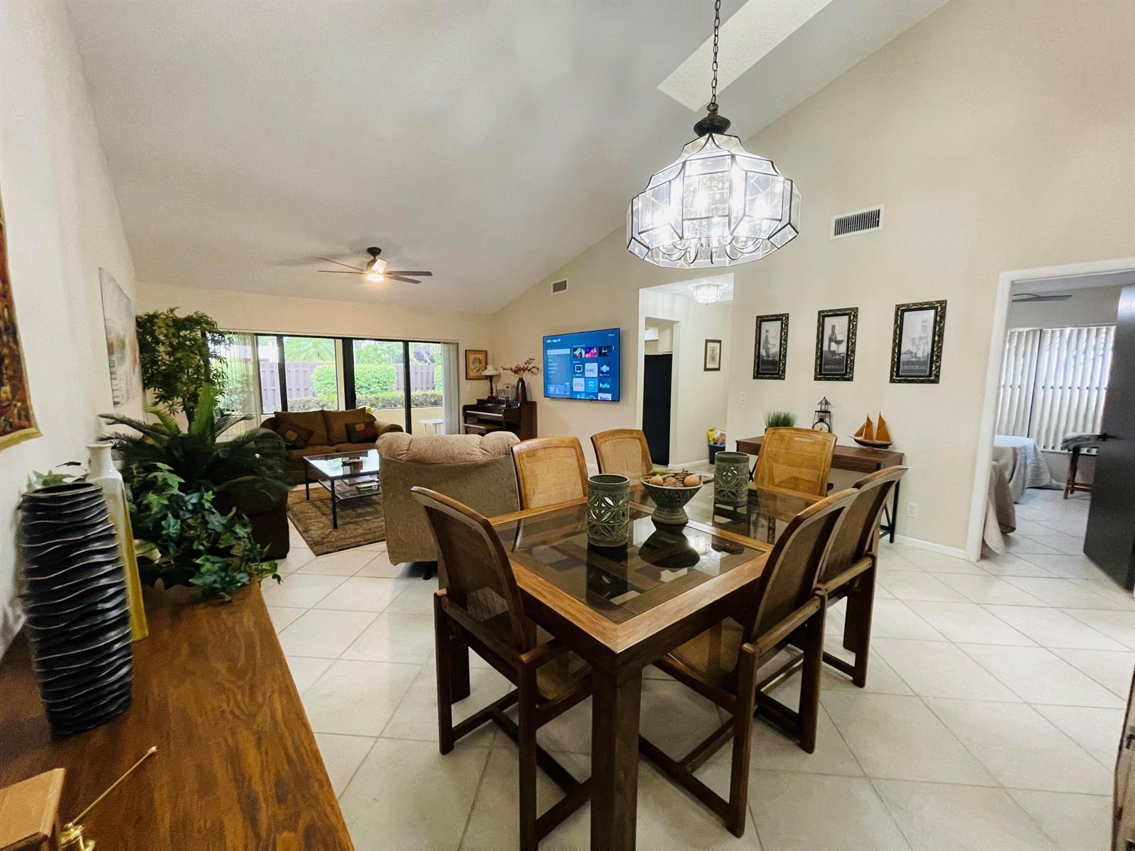 A dining area with a glass-top table and chairs sits before an open-concept living room — 354 SW 28th Avenue, Delray Beach FL 33445, DELRAY BEACH, FL