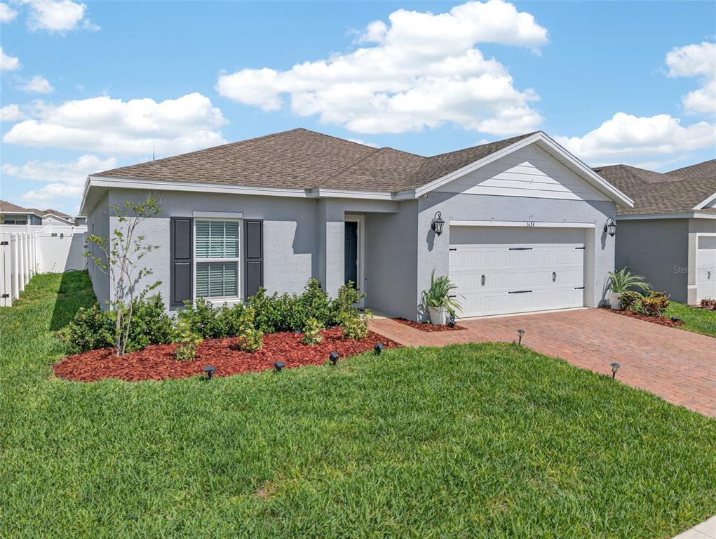 A single-story gray house with a brick driveway, two-car garage, and a manicured front lawn — 1654 LAIA ROAD, HAINES CITY, FL