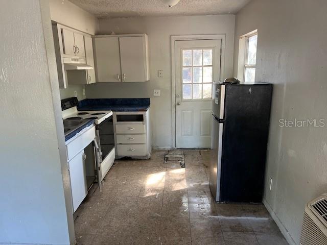 A kitchen with white cabinets, a black refrigerator, a stove, and worn flooring — 410 TERRY STREET, WILDWOOD, FL