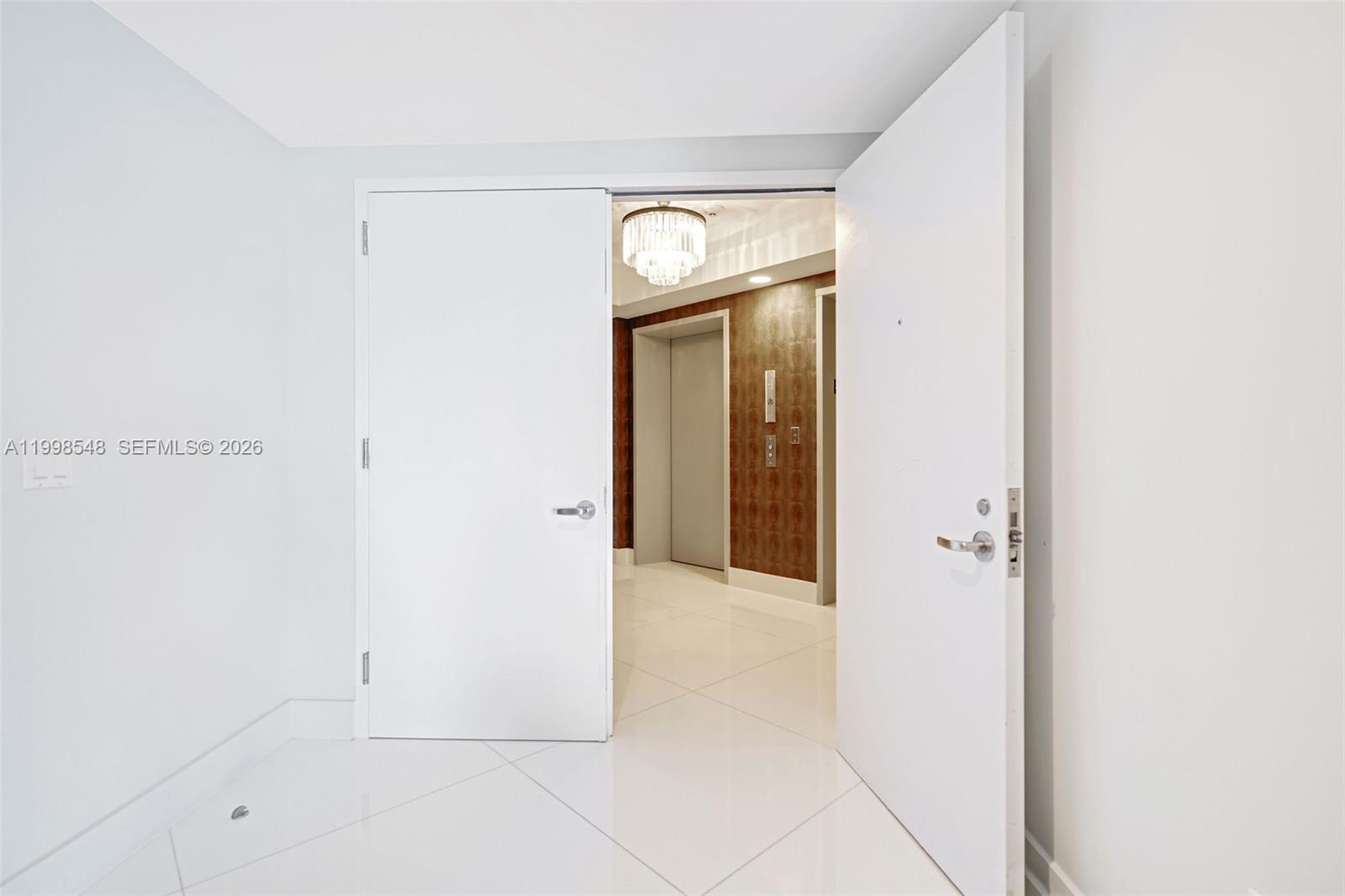An open doorway reveals a hallway with a chandelier, elevator doors, and patterned wallpaper — 2711 S Ocean Dr # 2803, Hollywood FL 33019, HOLLYWOOD, FL