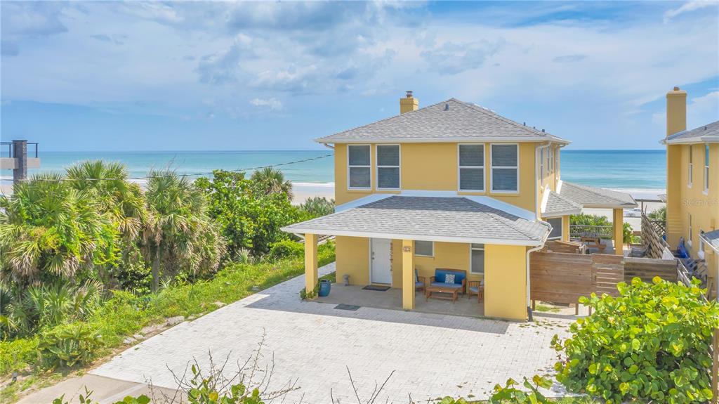 A yellow two-story house with a covered front porch sits near a sandy beach — 2101 HILL STREET, NEW SMYRNA BEACH, FL
