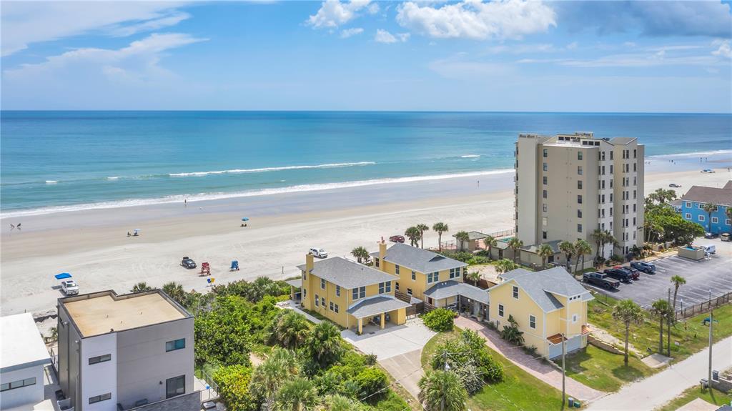 An aerial view shows yellow houses near a sandy beach and a tall apartment building — 2101 HILL STREET, NEW SMYRNA BEACH, FL