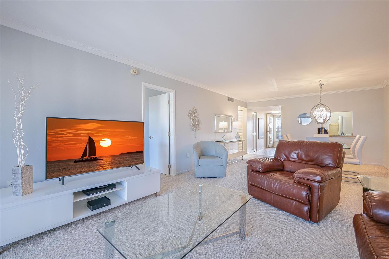 A living room features a television, leather armchairs, a glass coffee table, and carpeted floors — 3920 Inverrary Boulevard # c, Lauderhill FL 33319, LAUDERHILL, FL