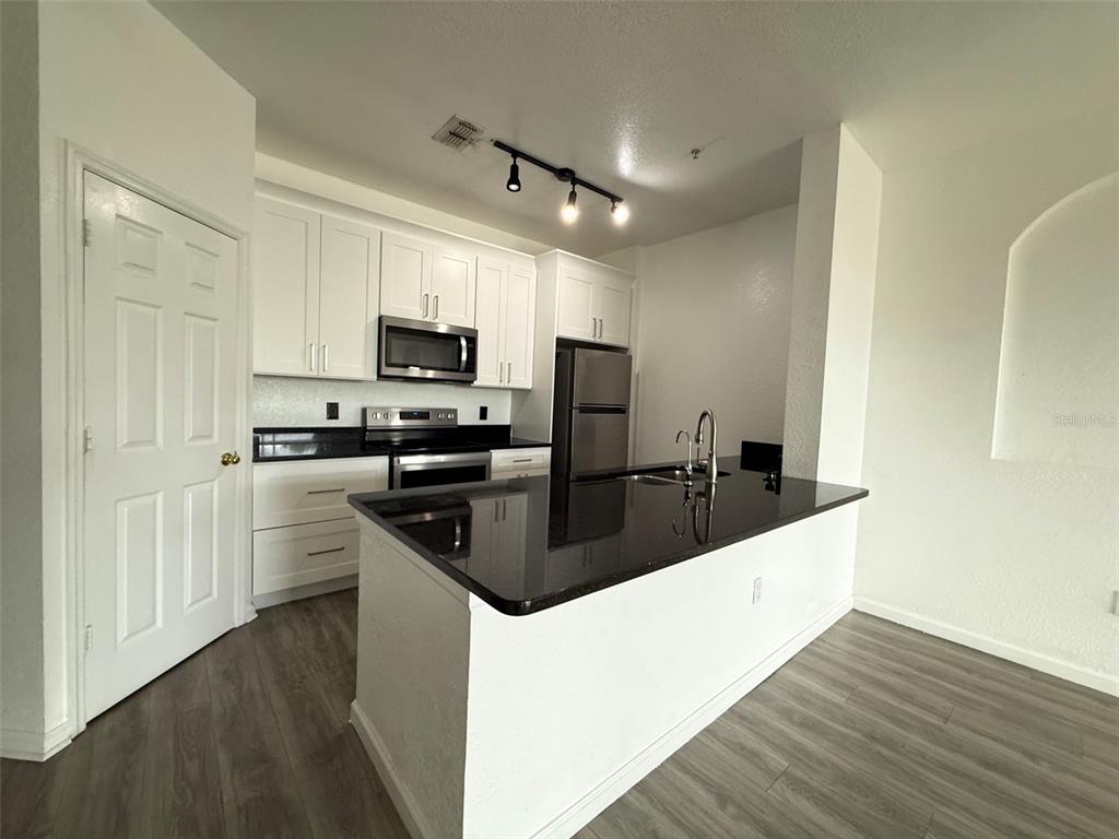 A kitchen features white cabinets, black countertops, stainless steel appliances, and wood-look flooring — 6380 CONTESSA DRIVE UNIT 303, ORLANDO, FL