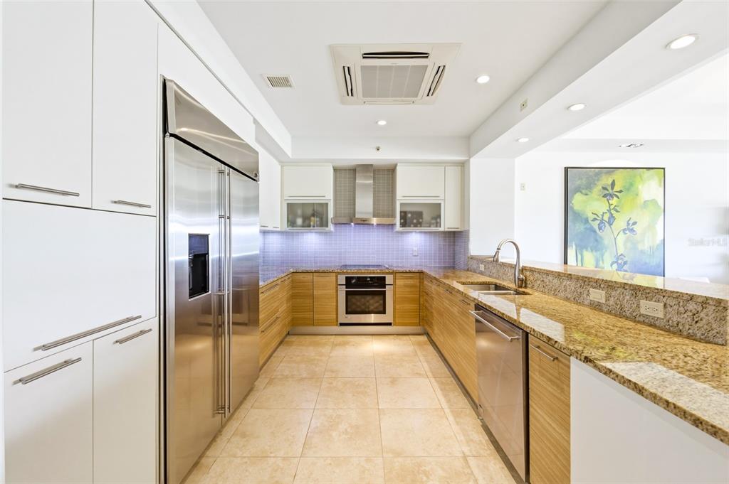A modern kitchen features stainless steel appliances, wood-toned lower cabinets, white upper cabinets, and granite countertops — PH 404 PLANTATION VILLAGE II UNIT 404, DORADO, PR