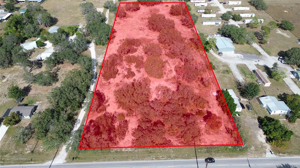An aerial view shows a rectangular, tree-covered vacant lot outlined in red along a road — JOHNSON AVENUE E, HAINES CITY, FL