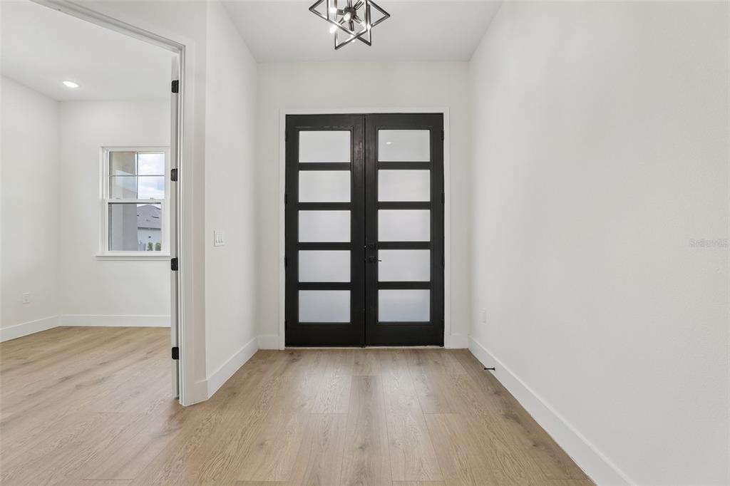 An entryway features light wood flooring, white walls, and a black double door with glass — 485 ADAMS VIEW LANE, AUBURNDALE, FL