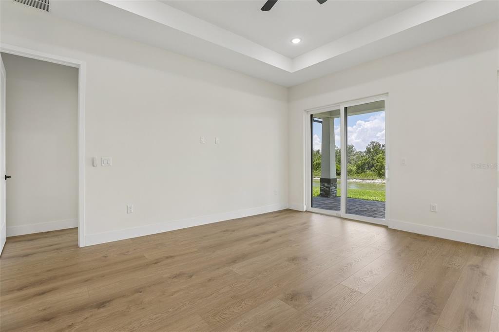 An empty bedroom features light wood flooring, a tray ceiling, and sliding glass doors — 485 ADAMS VIEW LANE, AUBURNDALE, FL