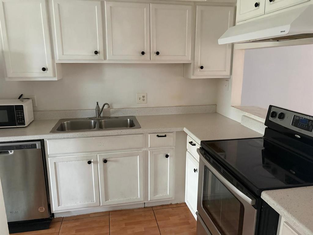 A kitchen features white cabinets, a stainless steel dishwasher, a black stove, and light countertops — 2320 MARGARITA COURT UNIT 2320, KISSIMMEE, FL