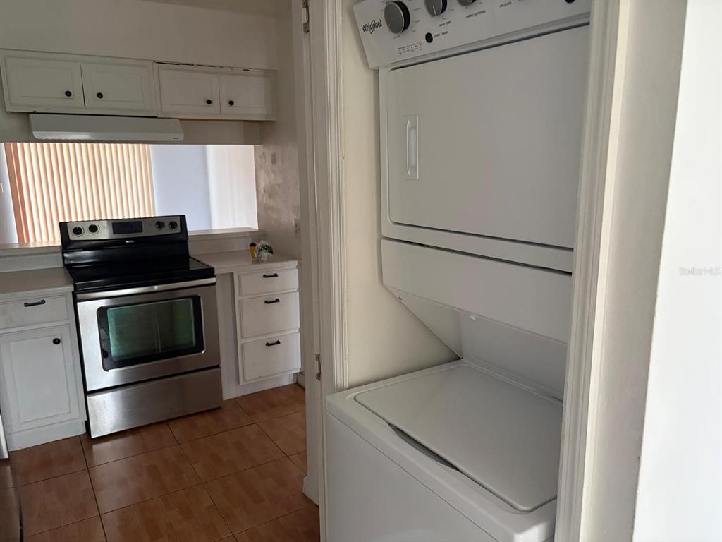 A kitchen features white cabinets, a stainless steel stove, and a stacked washer and dryer — 2320 MARGARITA COURT UNIT 2320, KISSIMMEE, FL