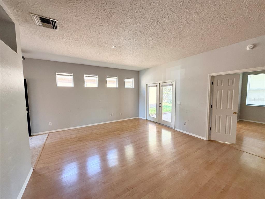 An empty living room with light wood flooring, four small windows, and glass patio doors — 112 PEREGRINE COURT, WINTER SPRINGS, FL