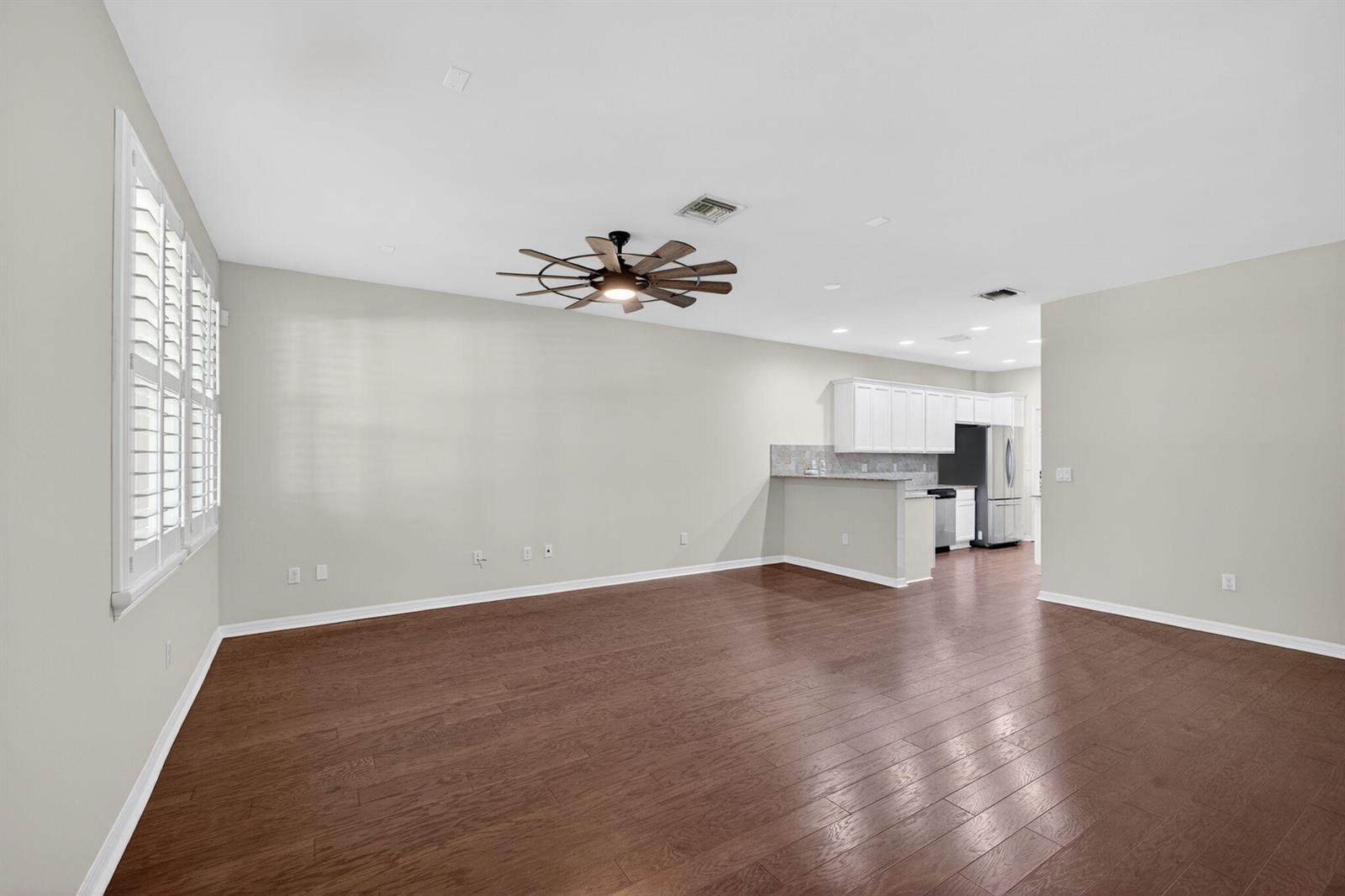 An open-concept living area features hardwood floors, a ceiling fan, and an adjacent kitchen — 1126 Dakota Drive, Jupiter FL 33458, JUPITER, FL