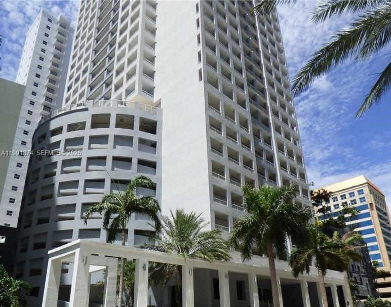 A low-angle view of a tall, white multi-story residential building with balconies and palm trees — 170 SE 14th St # 3005, Miami FL 33131, MIAMI, FL