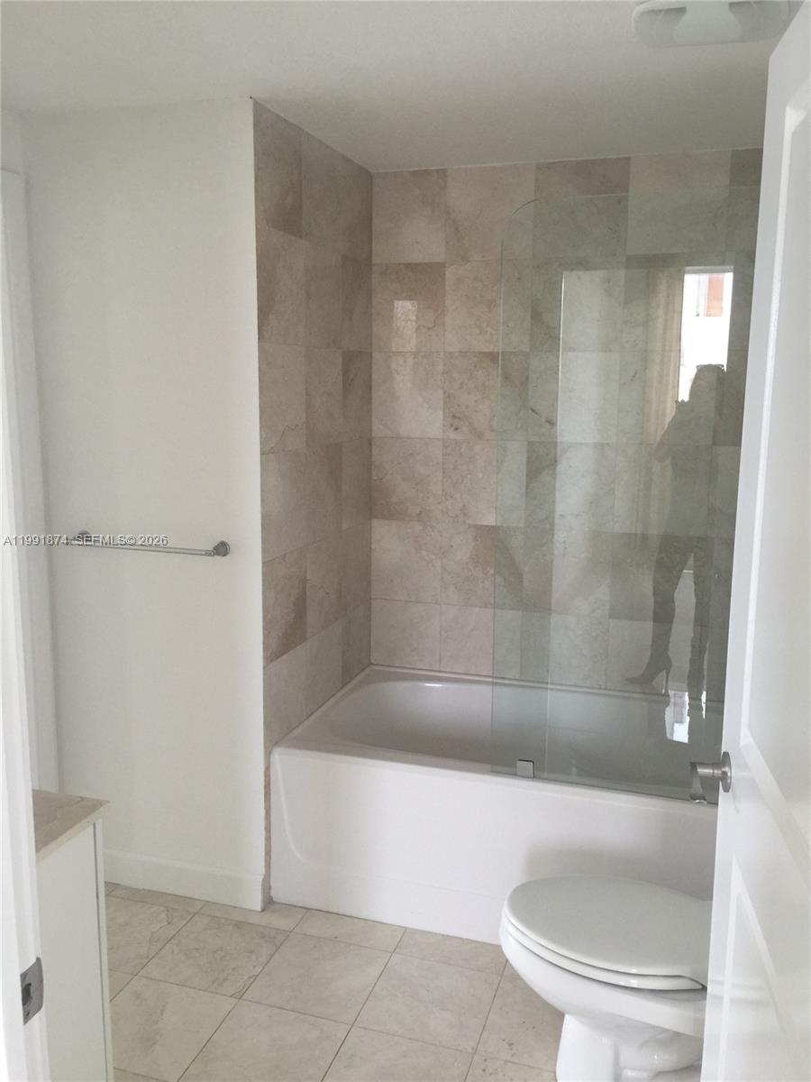 A bathroom features a white bathtub with a glass panel, beige tiled walls, and a toilet — 170 SE 14th St # 3005, Miami FL 33131, MIAMI, FL