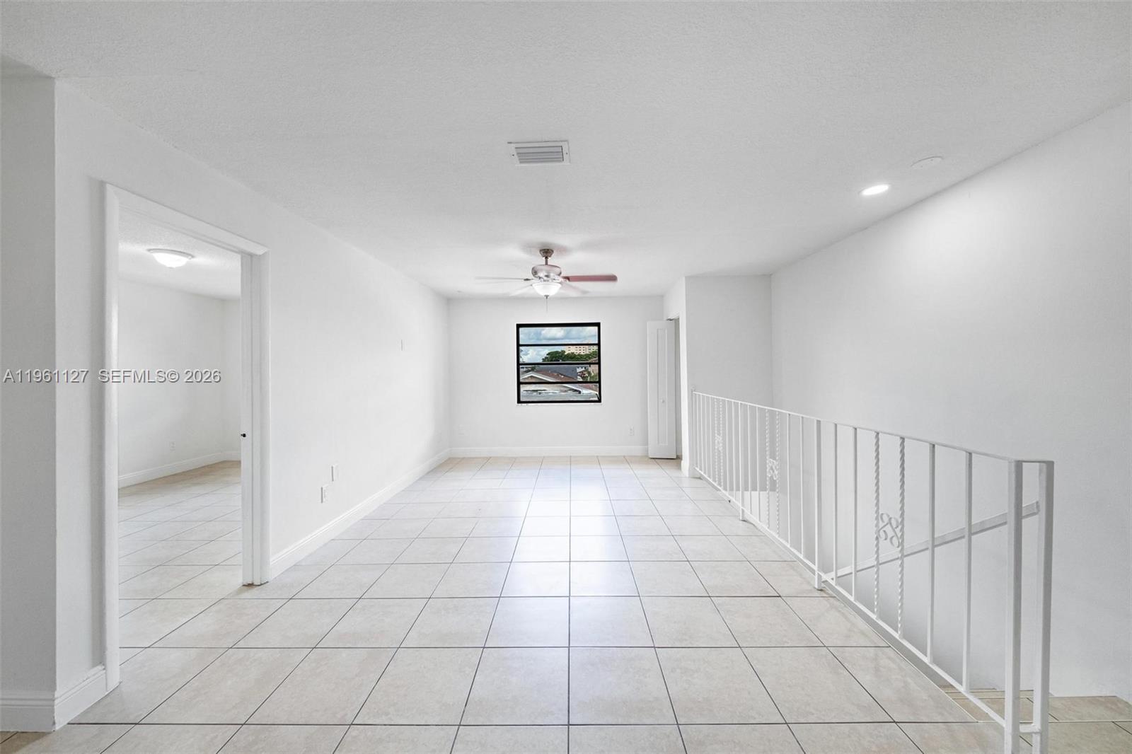 A bright, empty room features white walls, tiled floors, a ceiling fan, and a staircase railing — 1283 W 42nd St # 2, Hialeah FL 33012, HIALEAH, FL