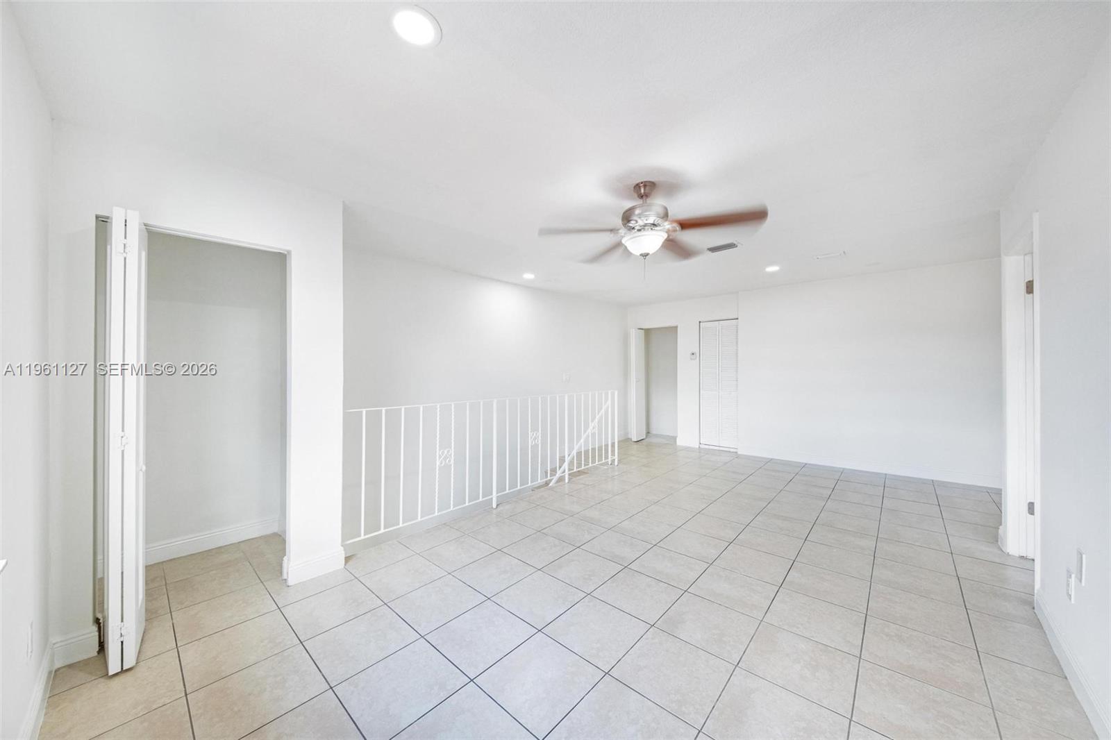 An empty room features white walls, tiled floors, a ceiling fan, and a stair railing — 1283 W 42nd St # 2, Hialeah FL 33012, HIALEAH, FL