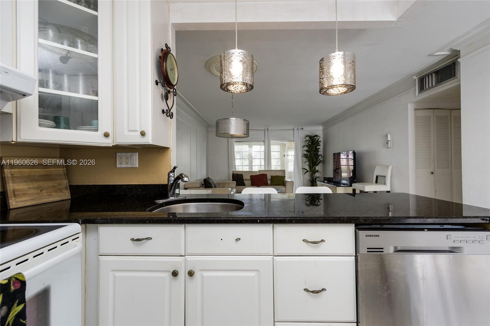 A kitchen with white cabinets and black countertops overlooks a living room with pendant lights — 4341 NW 16th St # 101, Lauderhill FL 33313, LAUDERHILL, FL