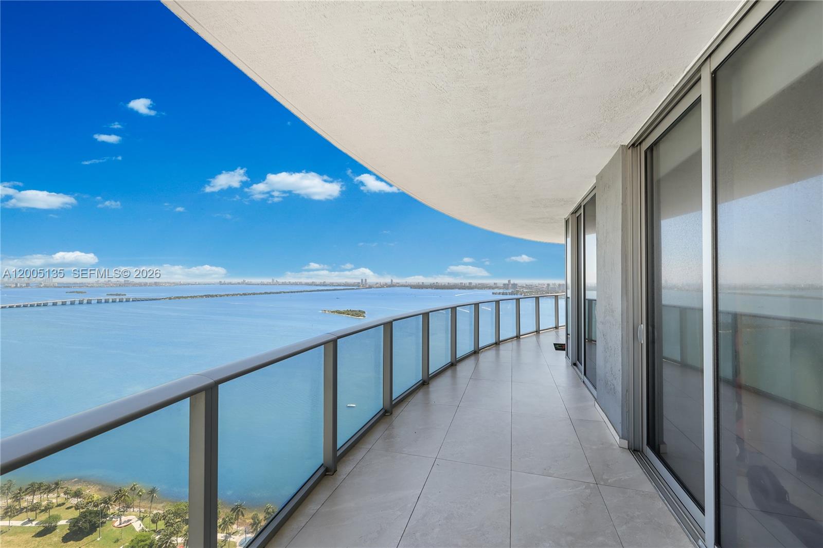 A curved balcony with glass railings overlooks a large body of water and city skyline — 488 NE 18th St # 3715, Miami FL 33132, MIAMI, FL
