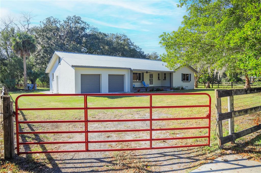 A red metal gate stands in front of a white house with a metal roof — 1850 NW 35TH STREET, OCALA, FL