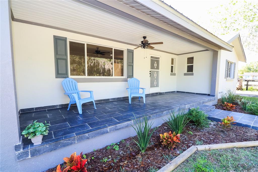 A covered front porch features dark tile flooring, two light blue chairs, and landscaping — 1850 NW 35TH STREET, OCALA, FL