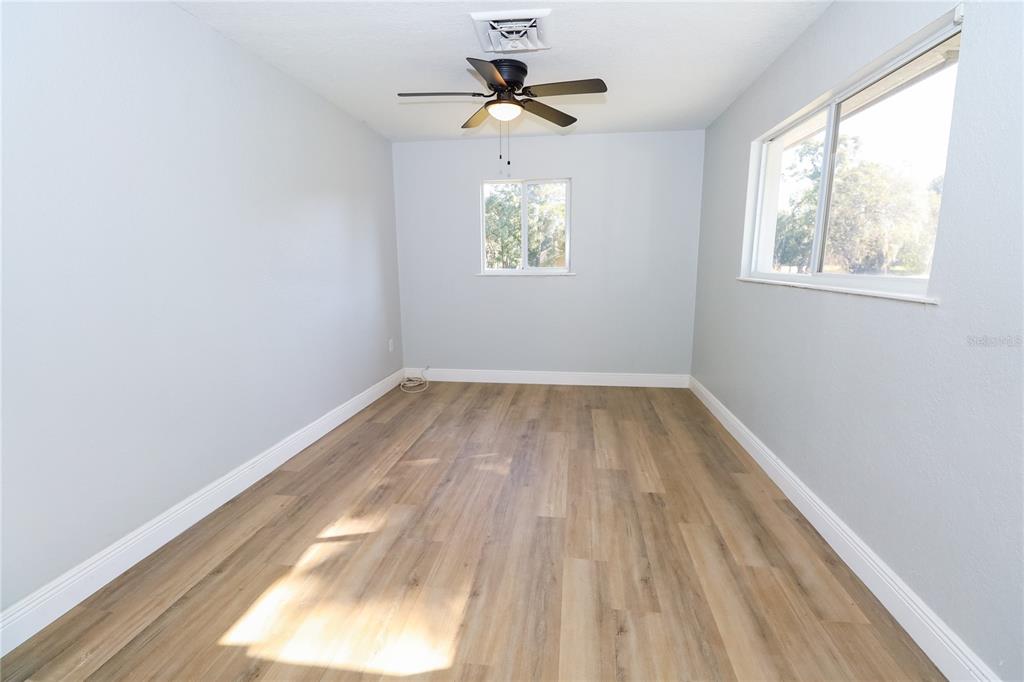 An empty bedroom features light gray walls, wood-look flooring, a ceiling fan, and two windows — 1850 NW 35TH STREET, OCALA, FL