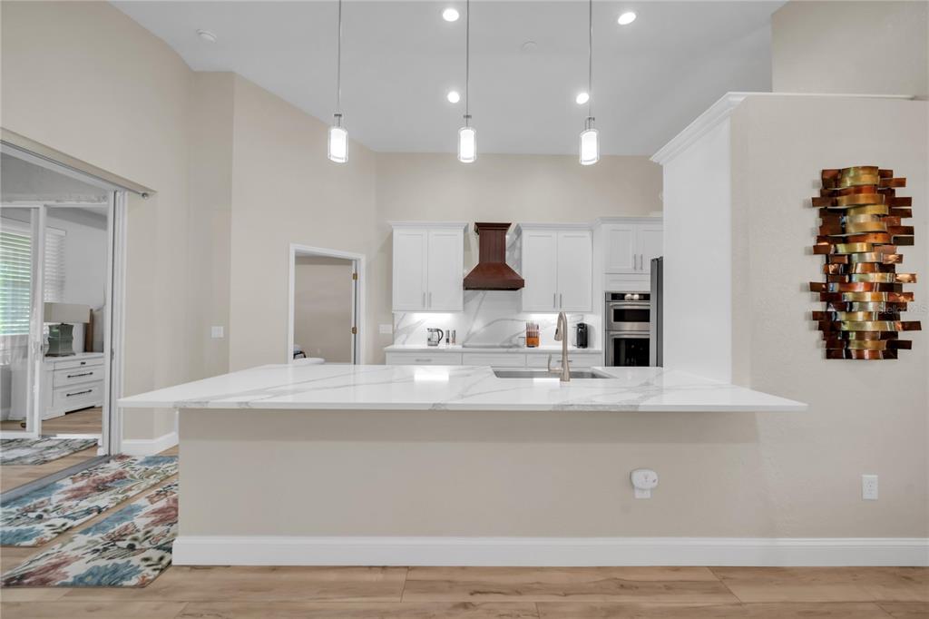 A kitchen features a white marble island, white cabinetry, a dark range hood, and pendant lighting — 1358 HEDGEWOOD CIRCLE, NORTH PORT, FL