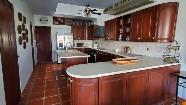 A kitchen features dark wood cabinets, a central island, and terracotta tile flooring — 27 SAN MIGUEL, HUMACAO, PR