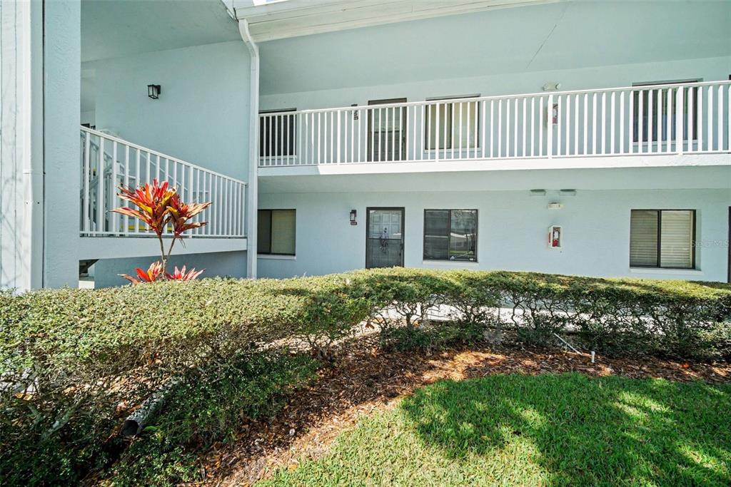 A two-story apartment building exterior with a white railing, landscaping, and a grassy lawn — 303 MARTHA LANE UNIT 303, OLDSMAR, FL