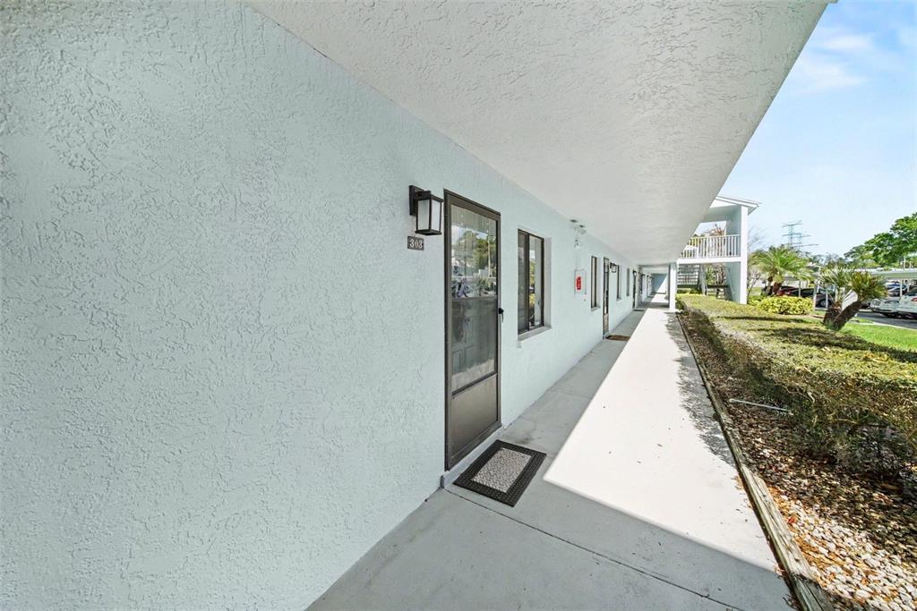 An exterior walkway leads past a row of apartment doors with light blue stucco walls — 303 MARTHA LANE UNIT 303, OLDSMAR, FL
