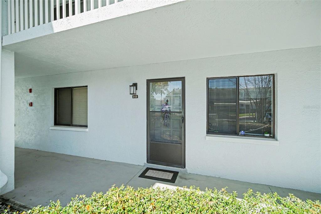 A ground-level apartment entrance features a screen door, two windows, and a concrete walkway — 303 MARTHA LANE UNIT 303, OLDSMAR, FL