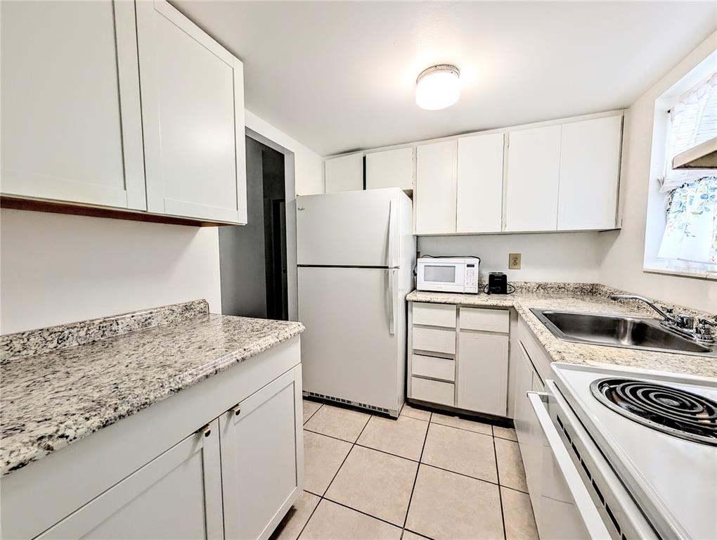 A kitchen features white cabinets, granite countertops, a white refrigerator, and tiled flooring — 5872 EASY STREET UNIT L2, BRADENTON, FL