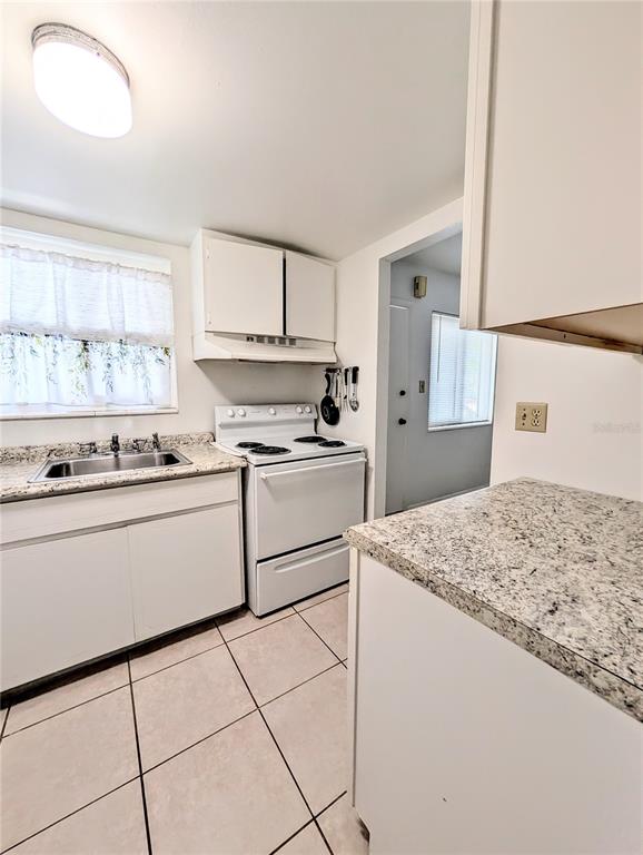 A kitchen features white cabinets, granite-look countertops, a white stove, and tiled flooring — 5872 EASY STREET UNIT L2, BRADENTON, FL