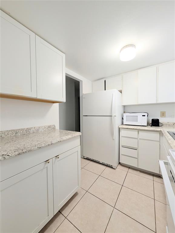 A kitchen features white cabinets, granite countertops, a white refrigerator, and light-colored tile flooring — 5872 EASY STREET UNIT L2, BRADENTON, FL