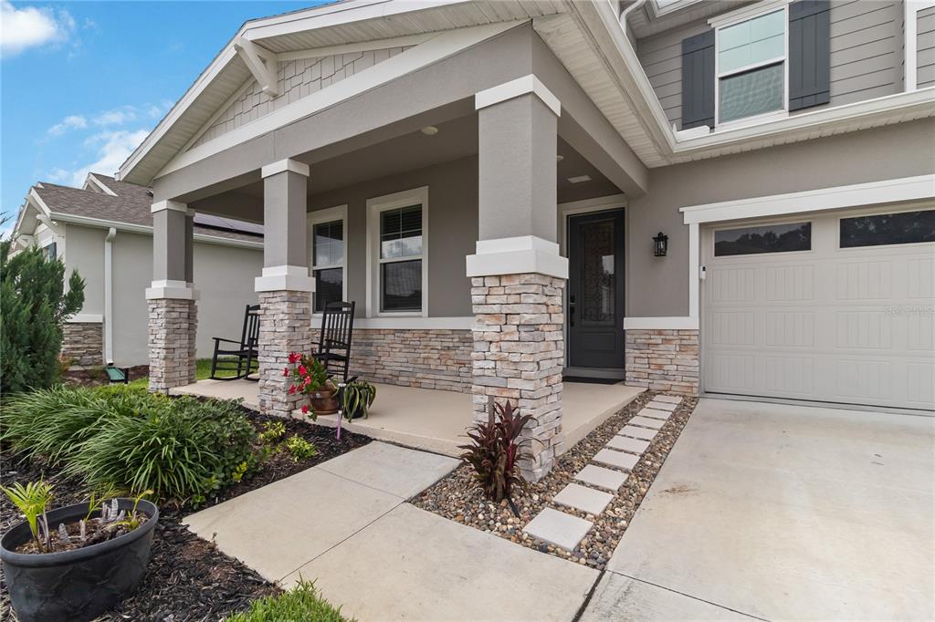 A house exterior features a covered front porch with stone pillars and a concrete driveway — 10105 SPRING LAKE DRIVE, CLERMONT, FL