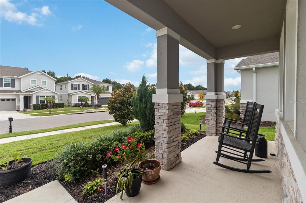 A covered front porch features stone-based columns, two black rocking chairs, and potted plants — 10105 SPRING LAKE DRIVE, CLERMONT, FL