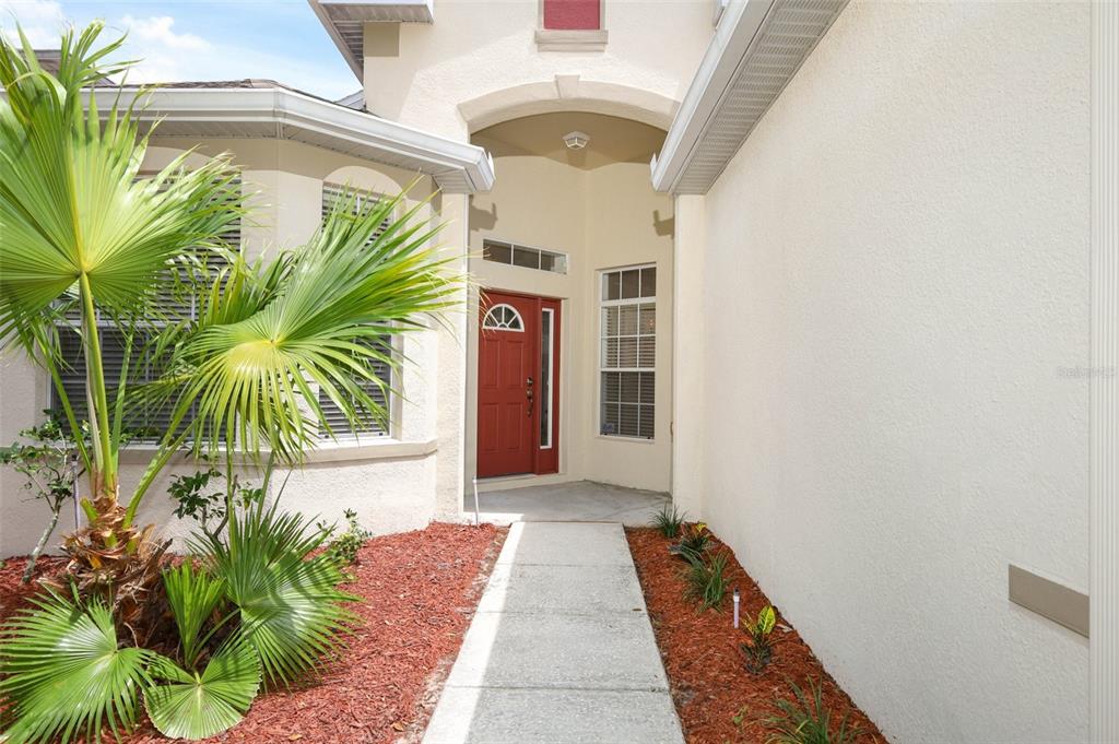 A concrete walkway leads to the red front door of a stucco house with landscaping — 5317 FLORENCE HARBOR DRIVE, ORLANDO, FL