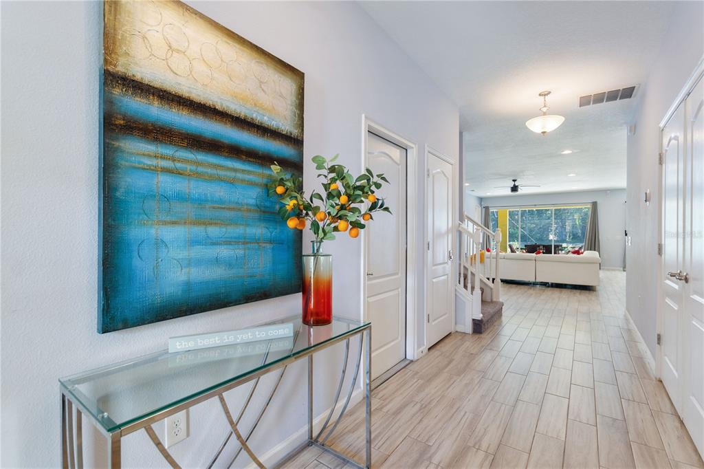 A bright entryway features a glass console table, abstract wall art, and light wood-look flooring — 5252 OAKBOURNE AVENUE, DAVENPORT, FL