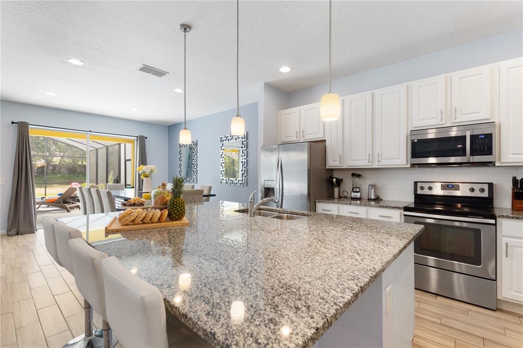 A kitchen with a granite-topped island, white cabinets, stainless steel appliances, and a dining area — 5252 OAKBOURNE AVENUE, DAVENPORT, FL