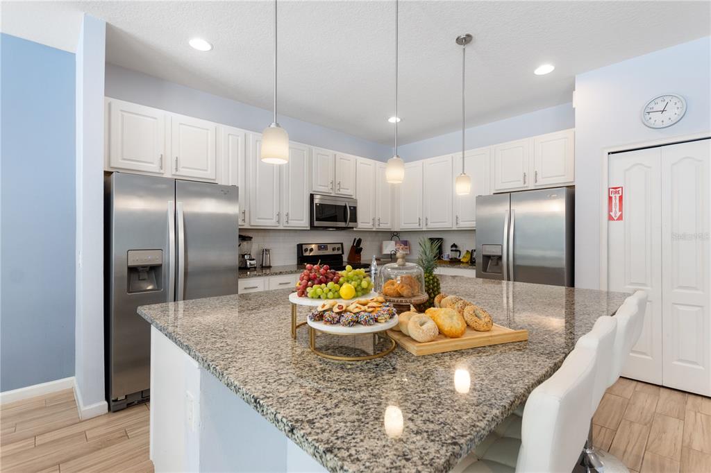 A kitchen features white cabinets, stainless steel appliances, granite countertops, and a large central island — 5252 OAKBOURNE AVENUE, DAVENPORT, FL
