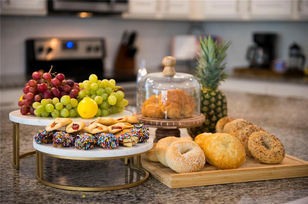 A kitchen island displays a variety of fresh fruit, pastries, and bagels on tiered stands — 5252 OAKBOURNE AVENUE, DAVENPORT, FL