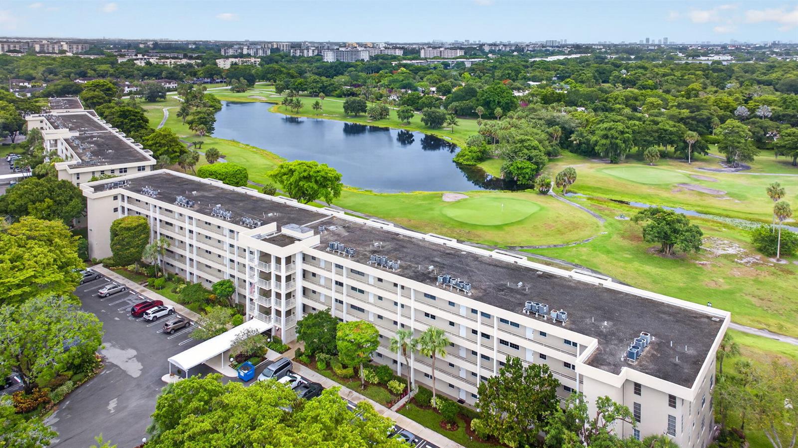 An aerial view shows a multi-story apartment building situated next to a golf course lake — 806 Cypress Boulevard # 209, Pompano Beach FL 33069, POMPANO BEACH, FL