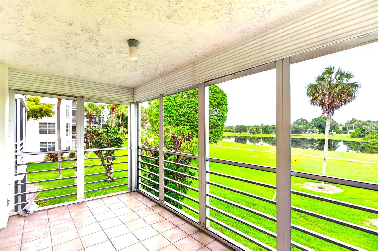 A screened-in balcony with tile flooring overlooks a grassy golf course and a pond — 806 Cypress Boulevard # 209, Pompano Beach FL 33069, POMPANO BEACH, FL