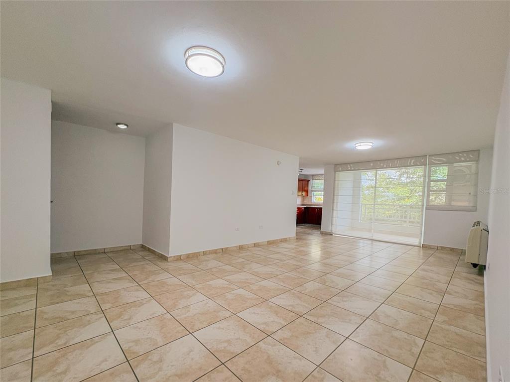 An open-concept living area features light-colored tile flooring, white walls, and a sliding glass door — 59 CLL UNION COND. HILLSVIEW PLAZA UNIT 107, GUAYNABO, PR