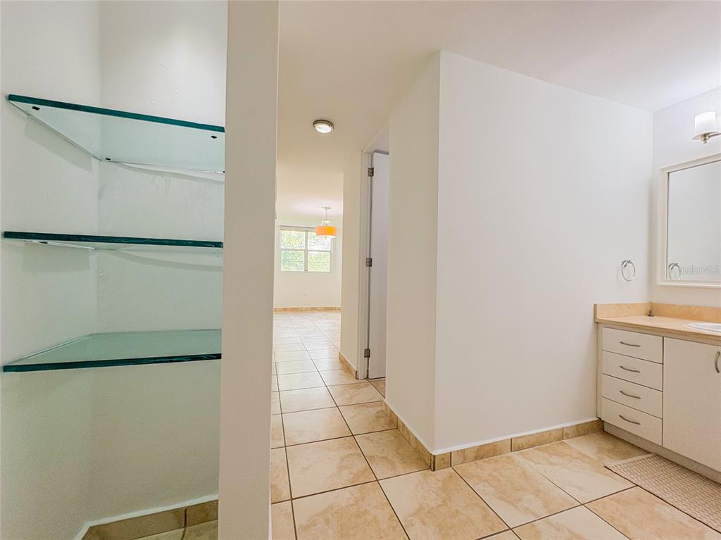 A bathroom with a vanity and glass shelving leads to a hallway with tiled floors — 59 CLL UNION COND. HILLSVIEW PLAZA UNIT 107, GUAYNABO, PR