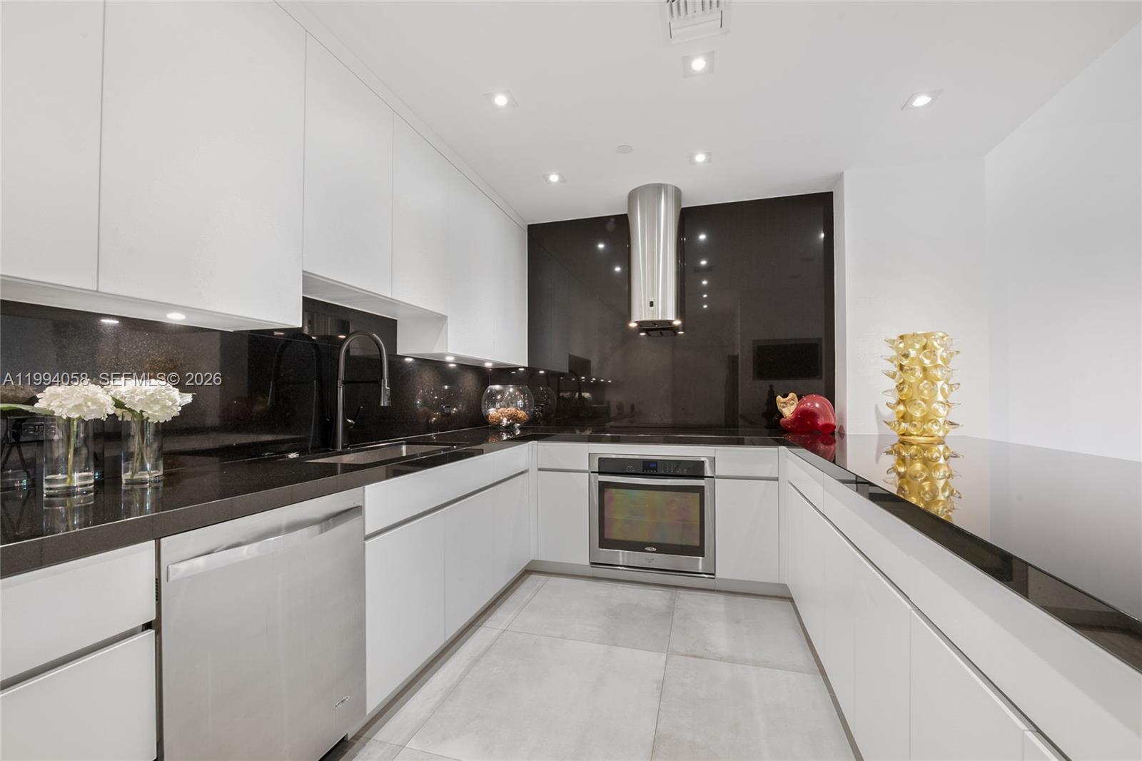 A modern kitchen features white cabinets, black countertops, a stainless steel oven, and tile flooring — 201 Crandon Blvd # 227, Key Biscayne FL 33149, KEY BISCAYNE, FL
