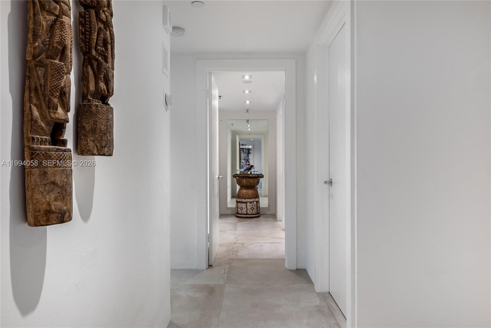 A white hallway features two wooden wall sculptures and a tiled floor leading to another room — 201 Crandon Blvd # 227, Key Biscayne FL 33149, KEY BISCAYNE, FL