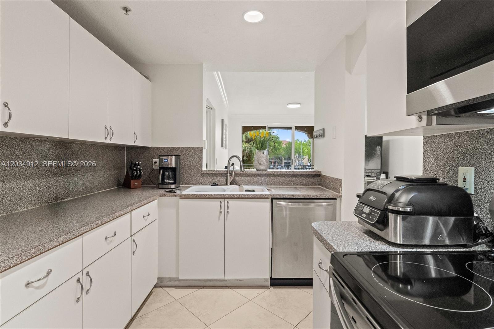 A kitchen features white cabinets, granite countertops, stainless steel appliances, and a pass-through window — 6540 NW 114th Ave # 1423, Doral FL 33178, DORAL, FL