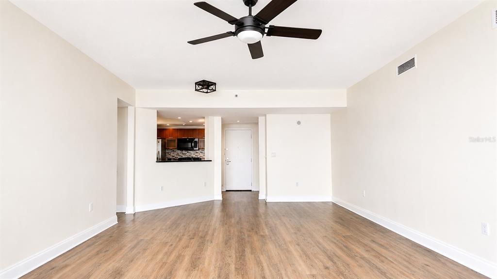 An empty living room with wood-look flooring, a ceiling fan, and an open kitchen view — 241 RIVERSIDE DRIVE UNIT 608, HOLLY HILL, FL