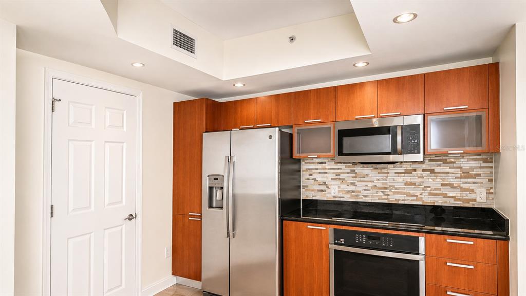 A kitchen features wood cabinets, stainless steel appliances, a tiled backsplash, and black granite countertops — 241 RIVERSIDE DRIVE UNIT 608, HOLLY HILL, FL