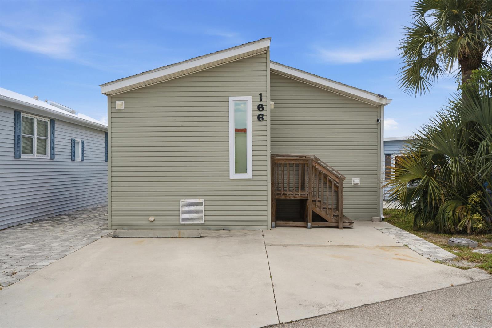 A light green mobile home exterior features a vertical window, house number, and wooden stairs — 166 Nettles Boulevard, Jensen Beach FL 34957, JENSEN BEACH, FL